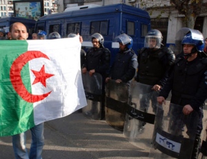 An Algerian protester holds an Algerian flag as he walks in front of Police officers during a demonstration in Algiers, Algeria, Saturday Feb. 12, 2011.  Some thousands of people defied a government ban on demonstrations and poured into the Algerian capital for a pro-democracy rally Saturday, a day after weeks of mass protests toppled Egypt's authoritarian leader. (AP Photo/Sidali  Djarboub)