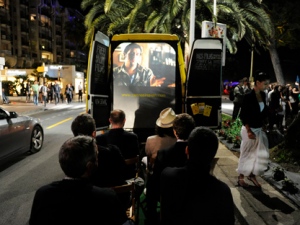 In this photo taken Tuesday, May 17, 2011, people watch a film projected onto a screen at the back of Andy Greenhouse's Cannes in a Van vehicle, at the 64th international film festival, in Cannes, southern France. The antithesis of the glitz of the Cannes Film Festival red-carpet premieres, Cannes in a Van offers spectators a folding chair, a glass of cheap wine and a variety of short films, from student efforts to prize winners. (AP Photo/Jonathan Short)