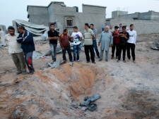 In this photo taken on a government organized tour local residents stand next to a crater with what appears to be a rocket parts in it, in Tripoli, Libya, on Sunday, June 5, 2011. Libyan officials claim that during a NATO airstrike a rocket targeted a nearby military site hit a residential area and damaged several houses. (AP Photo/Ivan Sekretarev)