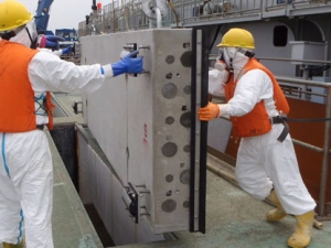 In this June 12, 2011 photo released on July 5, 2011 by Tokyo Electric Power Co., masked workers in protective outfits prepare to drop one of sliding concrete slabs into a slit of the upper part of the sluice screen for Unit 2 reactor at the tsunami-crippled Fukushima Dai-ichi nuclear power plant in Okuma, Fukushima Prefecture, northeastern Japan, in their effort to decrease the leak of radiation contaminated water to the ocean. (AP Photo/Tokyo Electric Power Co.)