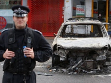 A police officer stands guard in front of a burned police car in Tottenham, north London, Sunday, Aug. 7, 2011 after a demonstration against the death of a local man turned violent and cars and shops were set ablaze. One police officer was hospitalized and seven others were injured during riots after a north London suburb exploded in anger Saturday night following a gathering to protest the Thursday shooting by police of the 29-year-old. (AP Photo/Akira Suemori)
