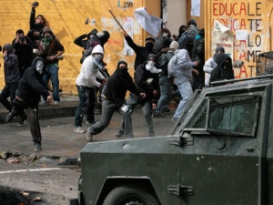 Masked demonstrators throw stones at riot police during clashes on the first day of a national strike in Santiago, Chile, Wednesday, Aug. 24, 2011. Chilean students, opposition politicians and union workers are leading a two-day nationwide strike to fight for fundamental changes in government. (AP Photo/Jose Miguel Rojas)