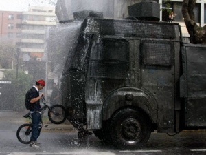 A biker tries to stop a police water canon during a demonstration of high school students outside the city hall in the neighborhood of Providencia in Santiago, Chile, Monday, Sept. 26, 2011. Students are on strike demanding more state funding to improve and guarantee free quality education to all Chileans. (AP Photo/Sebastian Silva)