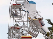 Two men and their ultra-light plane hang from a Ferris wheel while two children sit in a carriage near the top of the ride at a country festival at Old Bar, Australia, Saturday, Oct. 1, 2011. The four people were trapped in the tangled wreckage for hours after the plane crashed into the ride. (AP Photo/Carl Muxlow)