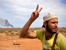 A Libyan revolutionary fighter gestures as smoke rises from the city of Sirte, Libya, Thursday, Oct. 6, 2011. Rebels used tanks and heavy artillery Thursday to fire on loyalist positions inside the home town of Libya's ousted leader Moammar Gadhafi. (AP Photo/Bela Szandelszky)