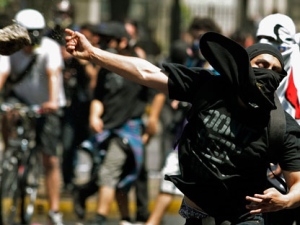 A masked protestor throws a stone at riot police in Santiago, Wednesday Oct. 19, 2011. Protestors manned flaming barricades and hurled bottles of flammable liquid at riot police on the second day of a two-day national strike called by students to protest against the government's education policies. The students have been demanding education reform since May and have set in motion another round of street protests after negotiations with the government broke down. (AP Photo/Luis Hidalgo)