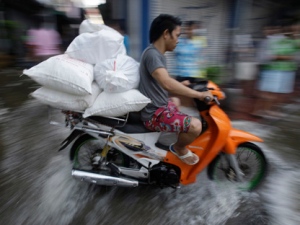 A man rides his motorcycle in a flooded street to deliver goods in Bangkok, Thailand on Friday, Oct. 28, 2011. The Chao Phraya river coursing through the capital swelled to record highs Friday, briefly flooding riverside buildings and an ornate royal complex at high tide amid fears that flood defenses could break and swamp the heart of the city. (AP Photo/Aaron Favila)
