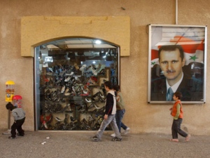 Syrian children pass next to a portrait of Syrian President Bashar Assad, in Barzeh suburb of Damascus, Syria, on Thursday Nov. 10, 2011. Syrian security forces raided homes and clashes erupted between soldiers and army defectors Thursday, killing at least 21 people across the country, including an 8-year-old girl and six soldiers, activists said. (AP Photo/Muzaffar Salman)