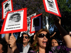 Human rights activists, holding up pictures of missing people, protest against an event honoring Miguel Krassnoff, a former Chilean army brigadier during the 1973-1990 dictatorship of August Pinochet, in Santiago, Chile, Monday, Nov. 21, 2011. Krassnoff is currently serving a 144-year sentence for homicide and forced disappearances. (AP Photo/Aliosha Marquez)