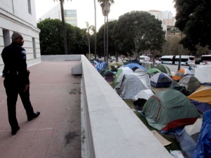 In this Nov. 2, 2011, photo, a Los Angeles police officer looks at tents set up outside Los Angeles City Hall in Los Angeles. Occupy LA, a 485-tent camp surrounding City Hall downtown, has marched to a different beat in its drum circle. Protesters, police and city officials early on established a relationship based on dialogue instead of dictate. As camps in other cities degenerated into unrest and led to mass arrests, Occupy LA has remained largely a bastion of peaceful pot smokers with city leaders determined that Los Angeles would emerge from the shadow of Rodney King once and for all. (AP Photo/Jae C. Hong, File)