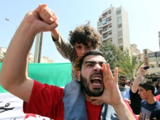 An Anti-Syrian regime protester carries his son and chant slogans against Syrian President Bashar Assad during a demonstration after Friday prayers in Beirut, Lebanon, Friday, April 6, 2012. Troops loyal to Syrian President Bashar Assad shelled two restive central cities and sent tanks and snipers into battle against rebels in the capital's suburbs on Friday, broadening an offensive that appeared aimed at crushing pockets of opposition less than a week before an internationally sponsored cease-fire is to take hold, activists said. (AP Photo/Bilal Hussein)