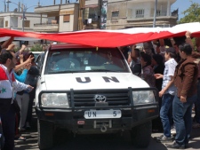 In this photo released by the Syrian official news agency SANA, a UN vehicle passes under a huge Syrian flag held by supporters of Syrian President Bashar Assad during observers' visit to the pro-Syrian regime neighborhoods in Homs province in central Syria on Monday, April 23, 2012. (AP Photo/SANA)