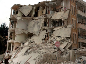 In this photo released by the Syrian official news agency SANA, a Syrian man stands in front of a building that was damaged after two bombs exploded near a military compound in the city of Idlib, Syria, Monday, April 30, 2012. (AP Photo/SANA) 