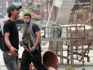 A Sunni gunman walks next to a man who reacts during clashes, in the northern port city of Tripoli, Lebanon, Sunday May 13, 2012. Sectarian violence linked to the unrest in neighboring Syria shook the northern Lebanese city of Tripoli on Sunday, with street clashes killing one soldier and two civilians, the state news agency said. Residents said running gunbattles broke out in the city Saturday and continued through the night primarily between a neighborhood populated by Sunni Muslims opposed to Syrian President Bashar Assad and another area with many Assad backers from his Alawite sect. (AP Photo/Hussein Malla)