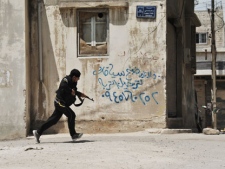 A Syrian rebel runs for cover at the Sunni district of Jabb al-Jandali in Homs, Syria, on Monday, May 14, 2012. Syrian troops shelled the rebel-held town, sparking intense clashes that sent bloodied victims flooding into hospitals and clinics, activists said. The violence around the country is eroding an internationally brokered peace plan that many observers see as the last hope to calm the 14-month-old crisis. Arabic writing on the wall is an advertisement. (AP Photo/Fadi Zaidan)