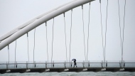 FILE - A woman makes her way across a bridge along the Lakeshore boardwalk taking cover from the rain in Toronto on Wednesday, May 18, 2011. THE CANADIAN PRESS/Nathan Denette 
