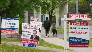 A person walks past multiple for-sale and sold real estate signs in Mississauga, Ont., on Wednesday, May 24, 2023. (The Canadian Press / Nathan Denette) 