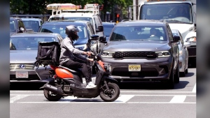 A delivery driver on a scooter rides the pedestrian crosswalk through traffic on a delivery in the Seaport District, Friday, June 7, 2024, in Boston. A soaring demand for food delivered fast has spawned small armies of couriers in a growing number of cities where delivery scooters, motorcycles and mopeds zip in and out of traffic and hop onto sidewalks alongside startled pedestrians racing to drop off salads and sandwiches. (AP Photo/Charles Krupa)