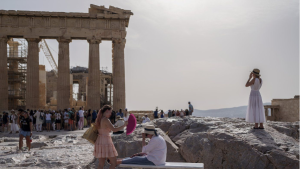 A tourist uses a hand fan to cool down another one sitting on a bench in front of the Parthenon at the ancient Acropolis, in Athens, Wednesday, June 12, 2024. AP Photo/Petros Giannakouris)