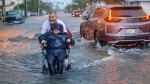 Victor Corone, 66, pushes his wife Maria Diaz, 64, in a wheelchair through more than a foot of flood water on 84th street in Miami Beach, Fla. on Wednesday, June 12, 2024. (AL Diaz / Miami Herald via AP)