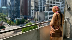 Shaheen Kauser stands on her balcony looking across the street at where a park has been replaced by construction. 