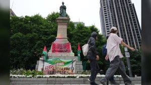 People walk past a defaced statue of Queen Victoria outside a new pro-Palestinian encampment set up on Square Victoria in downtown Montreal, Saturday, June 22, 2024. THE CANADIAN PRESS/Christinne Muschi