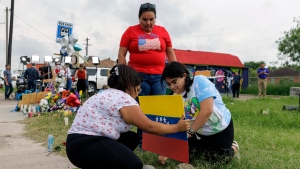FILE - Patty Limon watches her daughters Annaalexis Limon and Monica Limon place a Venezuelan flag, painted by Annaalexis, at a memorial where eight migrants were killed, and several others injured the day before while waiting at a bus stop in Brownsville, Texas, Monday, May 8, 2023. (AP Photo/Michael Gonzalez, File)