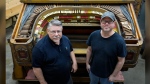 Carlton Smith, left, and Justin Nimmo pose in from of the console of the Barton Opus 234 theater organ that is undergoing restoration at Carlton Smith Pipe Organ Restorations in Indianapolis, Tuesday, July 2, 2024. The massive pipe organ built nearly a century ago for an extravagant movie house in Detroit is expected to be the centerpiece of a performing arts center at the Rochester Institute of Technology in Rochester, N.Y. (AP Photo/Michael Conroy)