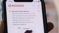 A person looks at their cell phone displaying a Rogers service interruption alert in Montreal on July 8, 2022. THE CANADIAN PRESS/Graham Hughes