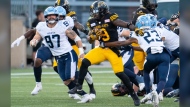 Hamilton Tiger Cats running back James Butler (9) breaks through the defensive line of the Toronto Argonauts during CFL football game action in Hamilton, Ont. on Saturday, July 20, 2024. THE CANADIAN PRESS/Peter Power