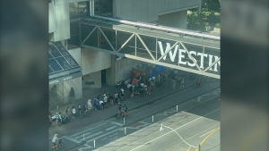 A long ferry lineup stretches out of the ferry terminal and onto the sidewalk on Queen's Quay West as people wait to get to the Toronto Islands Saturday July 20, 2024. (@AprilEngelberg /X)