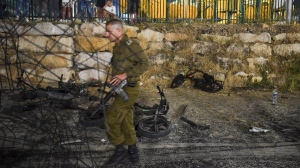 An Israeli military officer walks past destroyed children's bicycles at the site of a rocket attack in the Druze town of Majdal Shams, in the Israeli-controlled Golan Heights, Saturday, July 27, 2024. THE CANADIAN PRESS/AP , Gil Eliyah