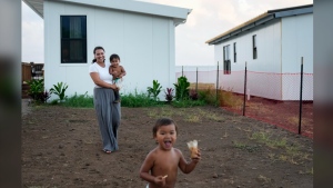 Josephine Fraser, 22, who was born and raised in Lahaina, holds her son Zyon Dias, 18 months, as she watches Ireh Dias, 3, front, run around outside their small home at Ke Ao Maluhia at the Maui Lani housing development, spearheaded by the Council for Native Hawaiian Advancement, Wednesday, July 10, 2024, in Kahului, Hawaii. The family has moved multiple times over the past 11 months after being displaced by the 2023 wildfire and are the first to move into the modular home community being built for those affected. (AP Photo/Lindsey Wasson)