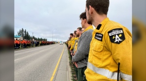 Comrades of a firefighter from Calgary who died while on duty in Jasper National Park stood on the sides of a roadway as a procession mourning his loss made its way past in Hinton, Alta., east of Japer National Park, on Sunday, Aug. 4, 2024. THE CANADIAN PRESS/HO-Alberta Wildfire