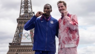 Erik Kynard of the United States, left, and Derek Drouin of Canada bite their London 2012 Olympic medals in the men's high jump during the Olympic medal reallocation ceremony, in Paris, France, Friday, Aug 9, 2024. (AP Photo/Michel Euler)