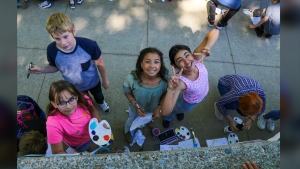 This photo provided by Spokane Public Schools shows Adams Elementary fifth graders pausing to pose for a photo while painting a mural at Spokane Community College, May 2024, in Spokane, Wash. (Spokane Public Schools via AP)