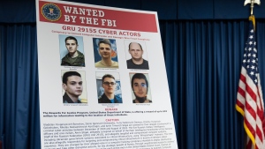 A graphic of the Russian suspects wanted by the FBI involved in a conspiracy to commit criminal cyber activities against Ukrainian government systems is displayed during a news conference at the Office of the United States Attorney in Baltimore, Thursday, Sept. 5, 2024. (AP Photo/Stephanie Scarbrough) 