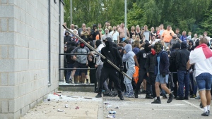 Thomas Birley, wearing a red scarf covering his face at centre right, gathers with others as windows are smashed outside the Holiday Inn Express in Rotherham, England on Aug. 4, 2024. (Danny Lawson / PA via AP)