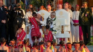 Pope Francis hugs a child in traditional dress, with East Timor's President José Manuel Ramos-Horta, seated at right, in Dili, East Timor on Sept. 9, 2024. (Gregorio Borgia / AP Photo)