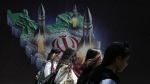 Iranian women without a mandatory headscarf, or hijab, walk past a banner showing missiles being launched from Iranian map in northern Tehran, Iran, April 19, 2024. (AP Photo/Vahid Salemi, File)