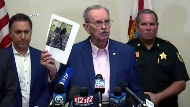 Palm Beach County Sheriff Ric Bradshaw holds up a photo that shows two backpacks hanging on a fence and a GoPro camera that were said to be near Donald Trump's golf club in West Palm Beach, Fla.