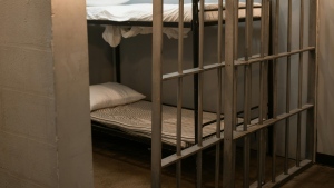 A jail bunk bed is shown behind bars (Pexels)