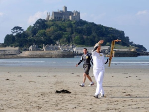 This photograph made available by LOCOG shows a torchbearer, no name given, carrying the Olympic torch on the beach, looking out to St Michael's Mount, during the leg of the torch relay between Newlyn and Marazion in south west England Saturday May 19, 2012. The torch will be carried all over the British Isles by 8,000 chosen volunteers, mostly local heroes. (AP Photo/Ben Birchall/LOCOG)