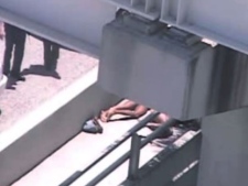 In this image taken from video, Miami police officers stand watch near a naked man, second from right, who was shot dead by a police officer when he refused to stop chewing on the face of the naked man next to him, partially obscured by a railing, on the MacArthur Causeway ramp onto Northeast 13th Street in Miami, Saturday, May 26, 2012. The victim was taken to a nearby hospital. Police say neither man's identity is known. (AP Photo/The Miami Herald) 